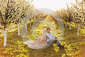 Enjoying time together. Beautiful young loving wedding couple in elegant wear sitting back to back on the green grass