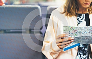 Enjoying travel. Young hipster smile girl with backpack traveling by train sitting near the window holding in hand and looking map