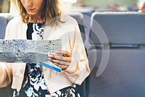 Enjoying travel. Young hipster smile girl with backpack traveling by train sitting near the window holding in hand and looking map