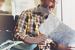 Enjoying travel. Young hipster smile man with backpack traveling by train sitting near the window holding in hand and looking map