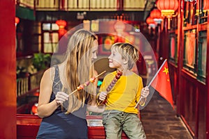 Enjoying vacation in China. Happy tourists mom and son with a Chinese flag and with traditional Chinese candied fruits