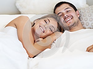 Enjoying waking up together. Smiling young couple lying in bed together.