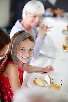 Enjoying yummy food with her family. a little girl having lunch with her family around the dining room table.