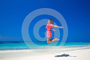 Enjoyment. Happy free woman jumping over sea and blue sky, brunette smiling girl in red dress on tropical beach. Enjoyment.