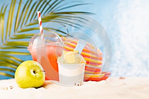 Enjoyment summertime - picnic on tropical beach with cold fruit cocktail, ice cream, sun hat under palm leaves with sand, sunny.