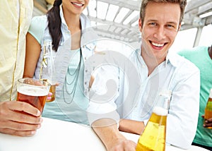 He enjoys a beer or two. Portrait of a handsome young man enjoying drinks on the outdoors deck of a restaurant.