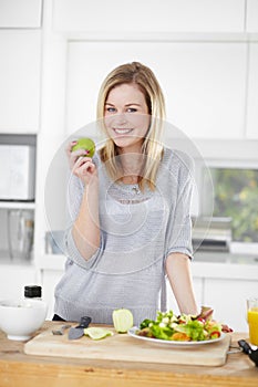 She enjoys healthy eating. Happy young woman making healthy food choices at home.