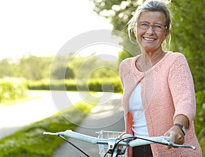 She enjoys healthy outdoor activities - Cycling. Smiling senior woman standing on a country lane with her bicycle.