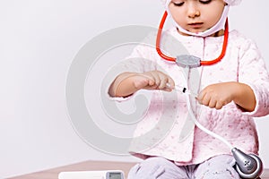 Enlarged photo of a preschool girl in a medical gown and mask with a syringe and a non-contact thermometer on a white