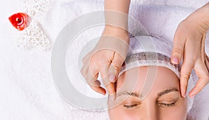 An enlarged photo of a woman with her eyes closed, who is doing a face and head massage. White towel and heart-shaped