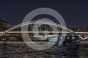 Enlightened Pedestrian Bridge at Night in Paris Seine River and Tourists Cruises