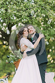 Enloved bride and groom in a park holding under tree decorated with many lanterns