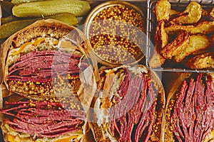 Enormous sandwiches with pastrami beef in wooden box. Served with baked potatoes, pickles