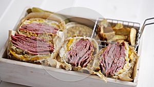 Enormous sandwiches with pastrami beef in wooden box. Served with baked potatoes, pickles