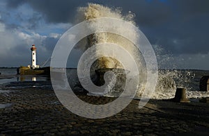 Enormous splash of water next to a lighthouse under the gloomy sky