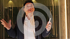 Enraged Angry Asian Business Man Going Up from Office Looking at Smartphone.