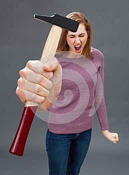 Enraged beautiful young woman shouting with hammer for DIY frustration