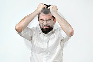 Enraged young businessman pulling his hair out for exasperation, having a burnout at work