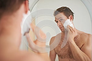 Ensuring a smooth shave. A handsome young man applying shaving cream to his face in front of a mirror.