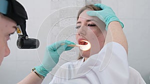 The ENT doctor examines the patient's oral cavity in the office of polyclinic with professional tools.