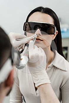 ENT doctor with laser treats girl patient in protective glasses. Laser treatment inflammation of the nasal lining, runny