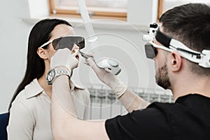 ENT doctor with laser treats girl patient in protective glasses. Laser treatment inflammation of the nasal lining, runny