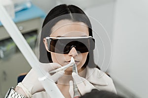 ENT doctor with laser treats girl patient in protective glasses. Laser treatment inflammation of the nasal lining, runny