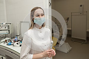 An ENT doctor in a modern ENT office of a hospital looks at the camera in a white coat and mask