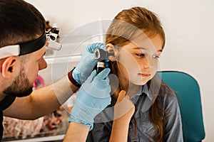 ENT doctor otolaryngologist looks through otoscope the ears of a little girl. Otoscopy. Treatment child ear pain.