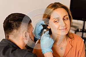 ENT doctor with otoscope. Otoscopy. Otolaryngologist looks through otoscope the ears of woman. Treatment ear pain.