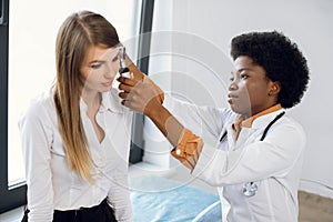 ENT doctor and patient in modern hospital. Female confident African American doctor doing ear examination with otoscope