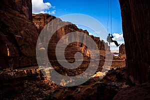 Entering a narrow canyon hanging in air, rappelling in Arches National Park, Utah