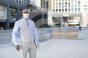 Enterprising black man on the street. He wears a face mask and holds a laptop under his arm