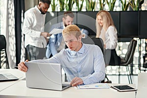 Enterprising caucasian office manager sitting at his workplace at office and studying report`s datas in the meeting room