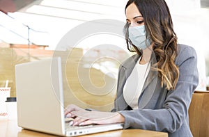 Enterprising young woman working with her laptop at her workplace. She is wearing a face mask and formal clothes. Selective focus