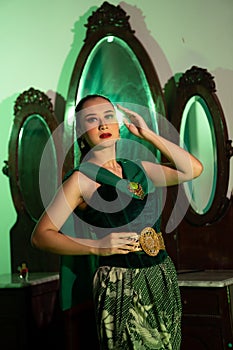 a entertainer woman with a green dress and scarf posing very beautiful and exotic in front of a makeup mirror in a green room