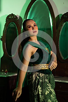 a entertainer woman with a green dress and scarf posing very beautiful and exotic in front of a makeup mirror in a green room