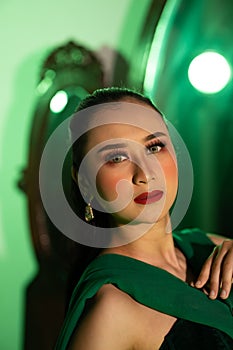 a entertainer woman with a green dress and scarf posing very beautiful and exotic in front of a makeup mirror in a green room