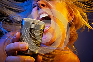 Entertaining female vocalist under gelled lighting sings with passion into condenser microphone