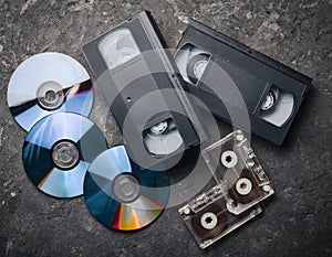 Entertainment and media technology from the 90s. CD& x27;s, audio cassettes, video cassettes on a black concrete surface.