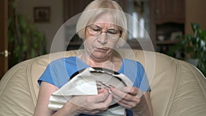 Enthralled concentrated good-looking senior woman sitting on chair at home cross stitching picture