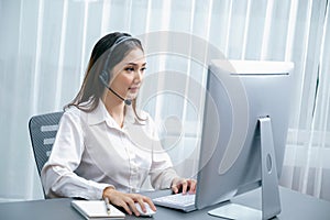 Enthusiastic asian call center with headset and microphone working on her laptop