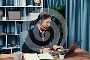 Enthusiastic asian call center with headset and microphone working on her laptop