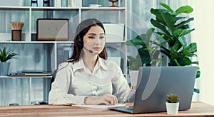 Enthusiastic asian call center with headset and microphone working on her laptop