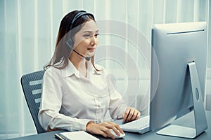 Enthusiastic asian call center with headset and microphone working on her laptop