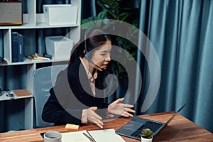 Enthusiastic asian call center with headset and microphone working on her laptop