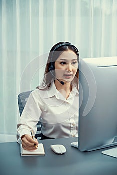 Enthusiastic asian call center with headset and microphone working on her laptop