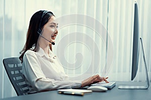 Enthusiastic asian call center with headset and microphone working on her laptop