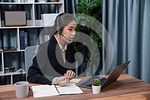 Enthusiastic asian call center with headset and microphone working on her laptop