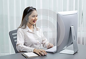 Enthusiastic asian call center with headset and microphone working on her laptop